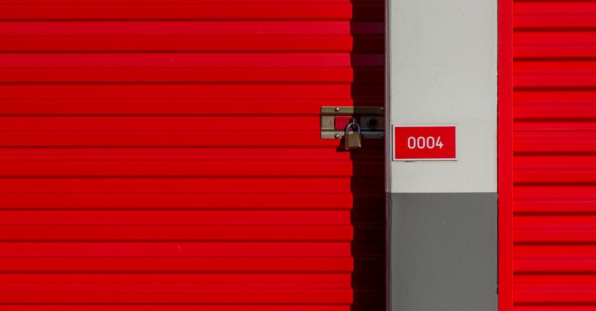 Red metal storage unit door with padlock and number 0004 sign on white panel.